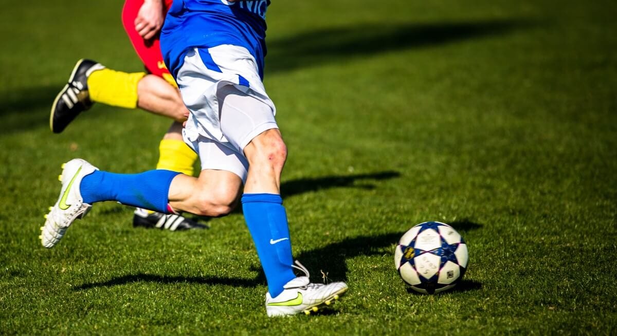 Football player dribbling match soccer ball on grass pitch, wholesale football ball manufacturer for club match balls